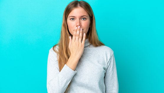 Woman standing against blue background, covering mouth