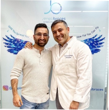 Orthodontist and patient taking a photo in front of orthodontic office logo