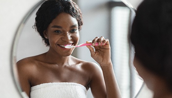 Woman smiling while brushing her teeth in bathroom
