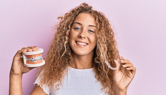 a teen holding up a model of a mouth with braces and clear aligners