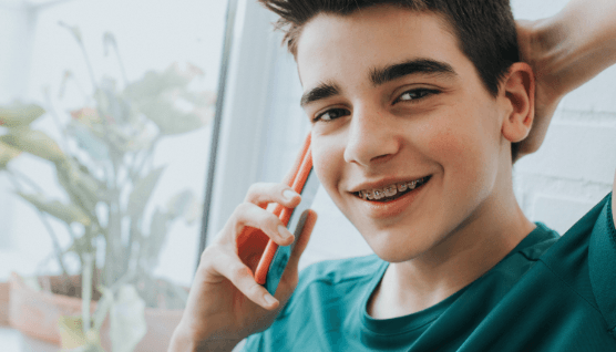 Smiling teen with braces on his cellphone