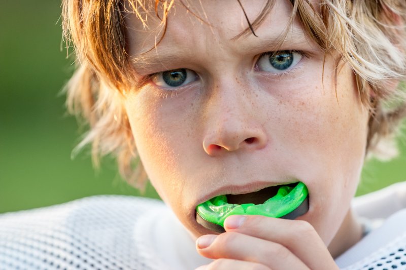 A boy in football pads putting in a mouthguard