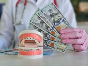 Person holding money behind model with dental braces